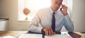 a professional male on a phone, looking at paperwork