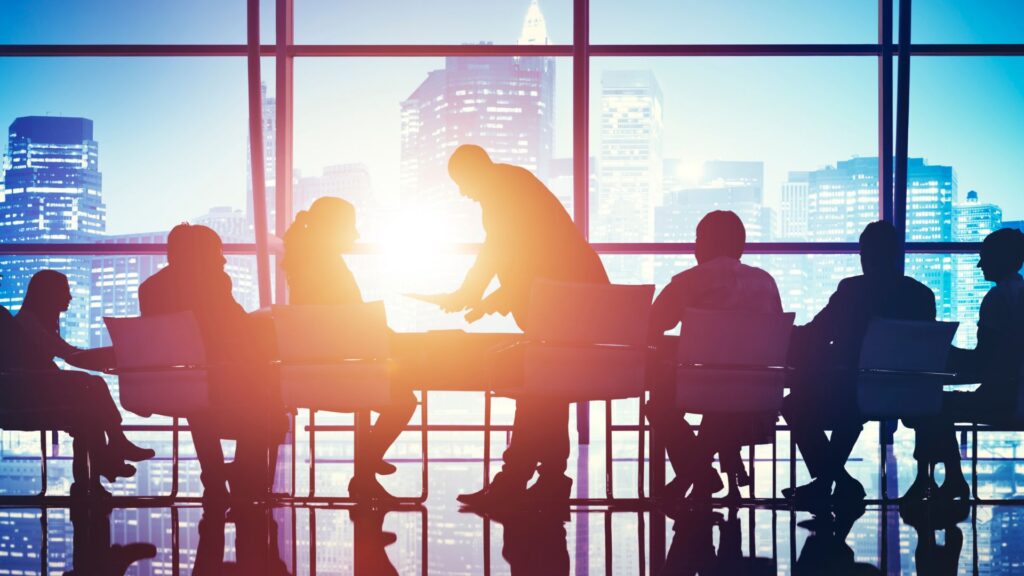 Silhouetted image of various professionals in a high-rise office against a cityscape backdrop at sunset