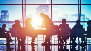 Silhouetted image of various professionals in a high-rise office against a cityscape backdrop at sunset