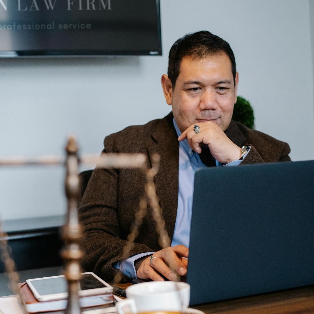 man in suit sits at table with laptop