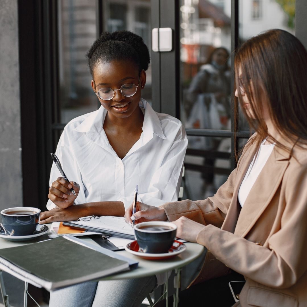 woman sit side by side at table with coffee