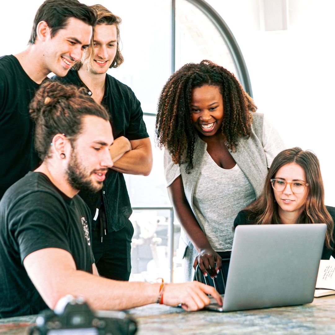 team of people standing around laptop on table