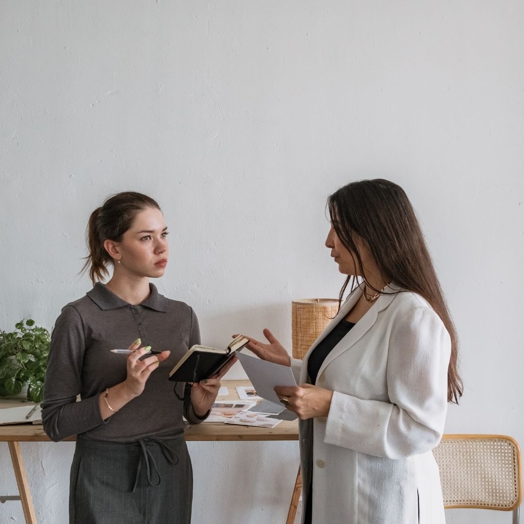woman in white coat talks to woman holding notebook